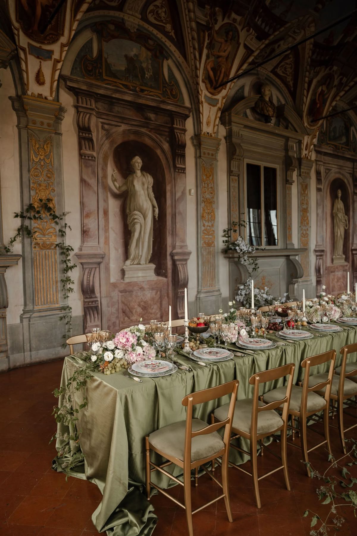 Long banquet table set with sage linen and candles inside a frescoed Italian hall